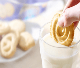 Hand dipping a cookie into a glass of milk.