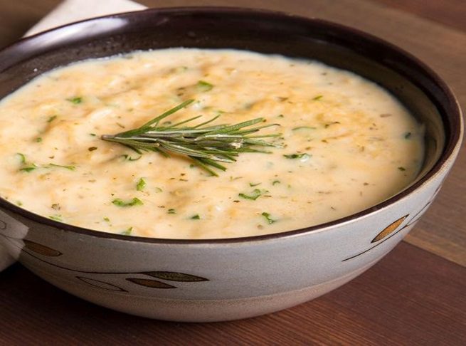 Creamy soup with rosemary garnish in a bowl.