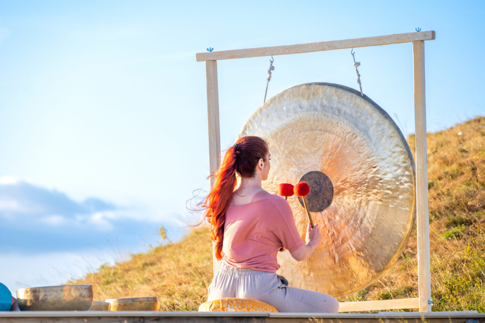 Sound therapy, woman hitting bronze gong, back side view. Traditional tibetan meditation, zen, harmony, relaxation concept